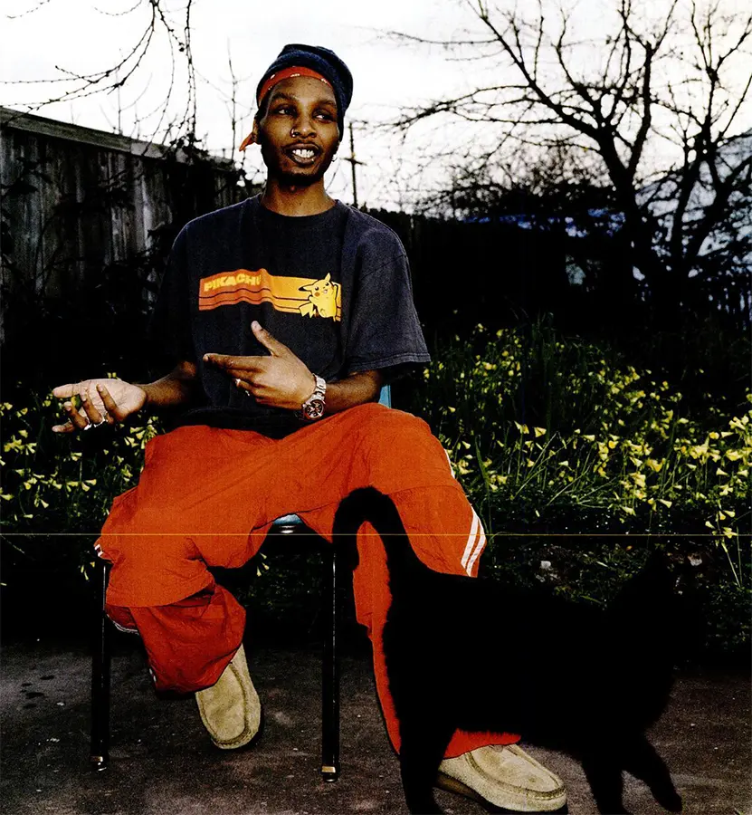 Del the Funky Homosapien sites in his backyard, while his cat brushes by his leg.